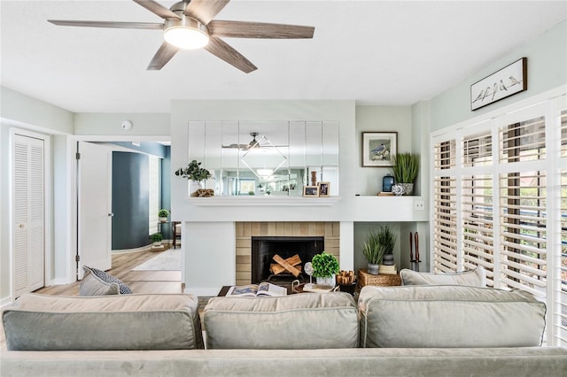 living area featuring baseboards, a ceiling fan, wood finished floors, and a fireplace