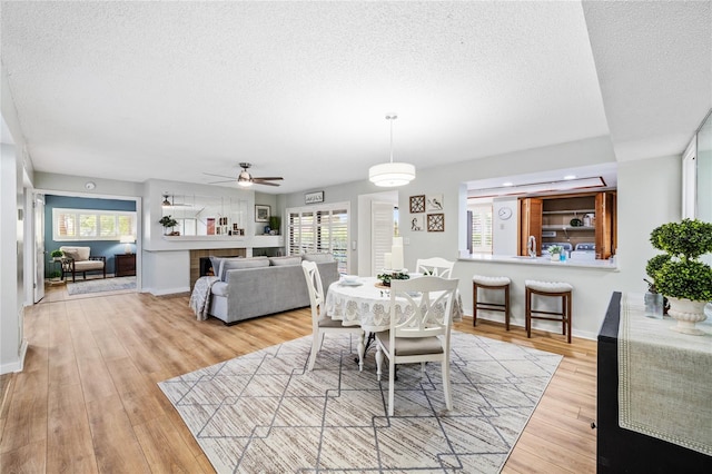 dining room featuring a textured ceiling, ceiling fan, light wood finished floors, and baseboards