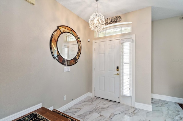 entryway with marble finish floor, an inviting chandelier, a wealth of natural light, and baseboards