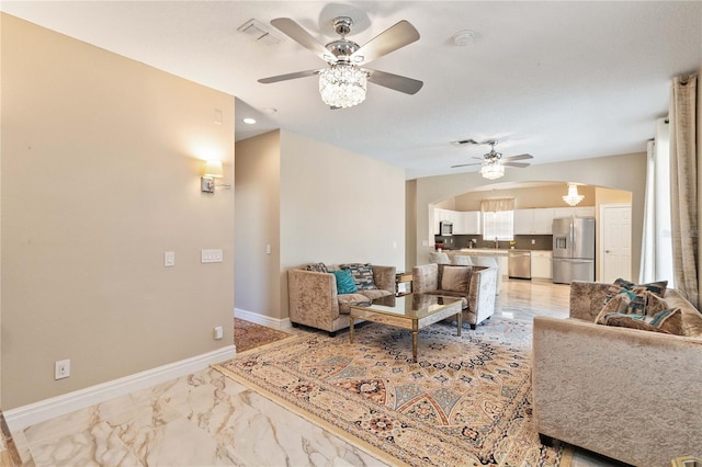 living area with a ceiling fan, arched walkways, marble finish floor, and baseboards