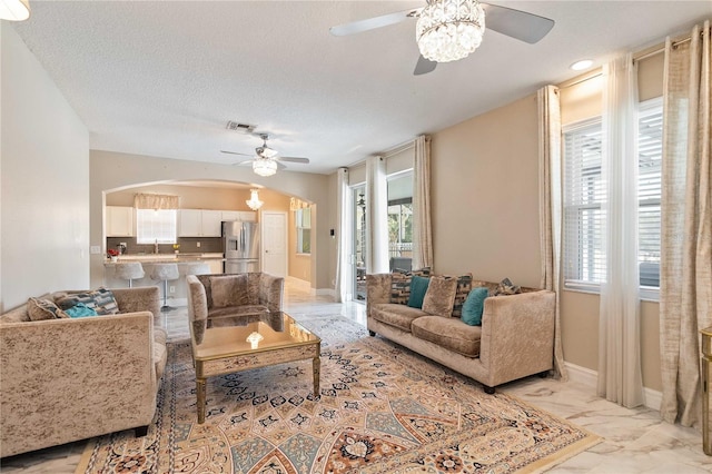 living room with arched walkways, ceiling fan, and a healthy amount of sunlight