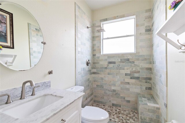 bathroom featuring a tile shower, toilet, and vanity