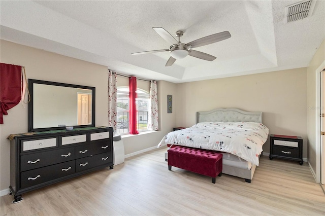 bedroom featuring a textured ceiling, a raised ceiling, visible vents, baseboards, and light wood finished floors