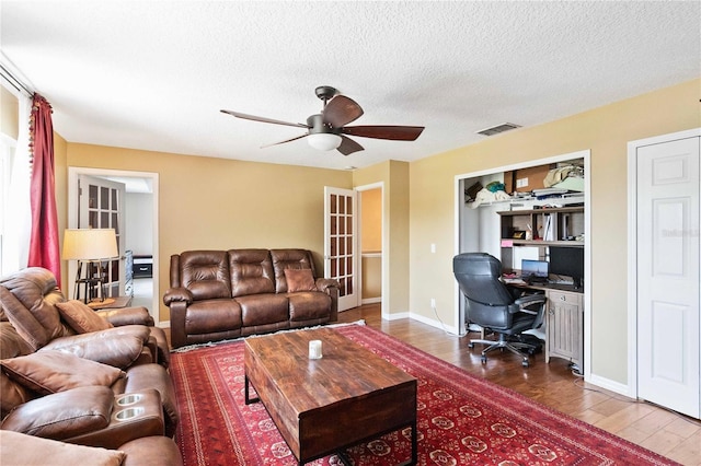 living room featuring visible vents, wood finished floors, ceiling fan, and a textured ceiling