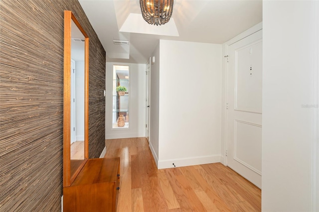 corridor featuring baseboards, a notable chandelier, light wood finished floors, and visible vents