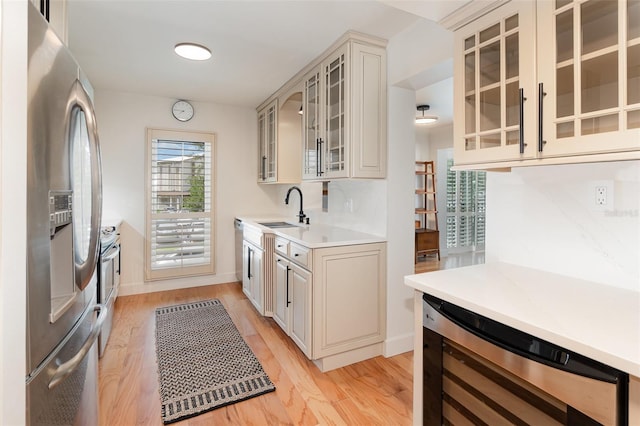 kitchen with beverage cooler, stainless steel appliances, light countertops, a sink, and light wood-style floors