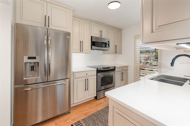 kitchen featuring light countertops, appliances with stainless steel finishes, cream cabinetry, and a sink
