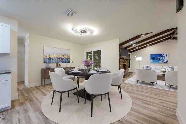 dining space featuring vaulted ceiling with beams, visible vents, baseboards, light wood-style floors, and a stone fireplace