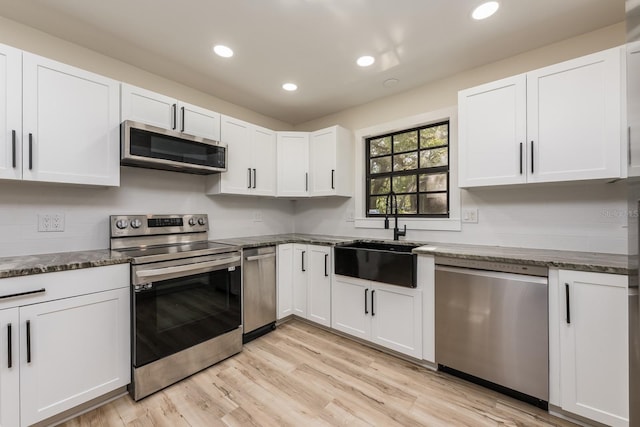 kitchen with recessed lighting, stainless steel appliances, dark stone countertops, a sink, and white cabinetry