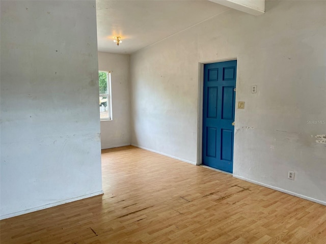 empty room featuring wood finished floors, baseboards, and lofted ceiling with beams