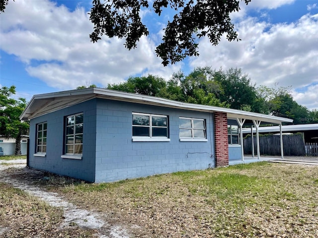 view of side of property with fence, concrete block siding, a yard, and an attached carport
