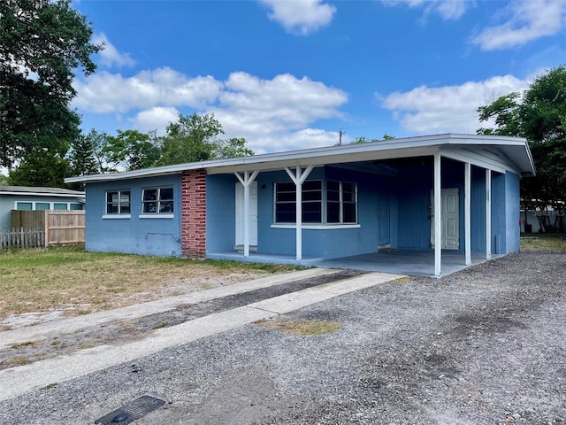 ranch-style home with fence, concrete block siding, a carport, and covered porch