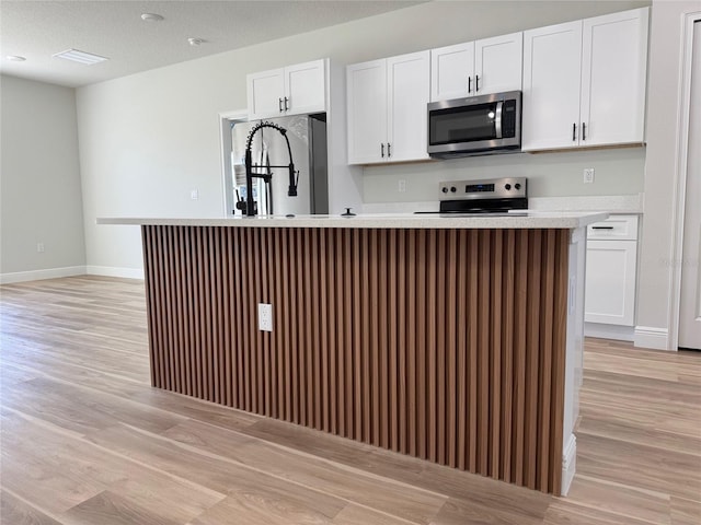 2406 SW 163rd Pl, Ocala, FL 34473 - kitchen featuring stainless steel appliances, light wood-type flooring, white cabinets, and a center island with sink