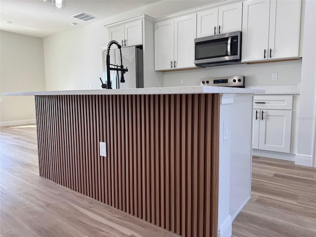 2406 SW 163rd Pl, Ocala, FL 34473 - kitchen with stainless steel microwave, light wood finished floors, white fridge, white cabinetry, and range