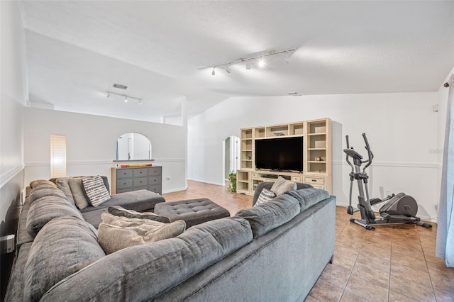 living room featuring arched walkways, vaulted ceiling, baseboards, track lighting, and light tile patterned floors