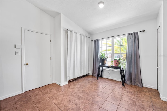 unfurnished room featuring vaulted ceiling, light tile patterned flooring, a textured ceiling, and baseboards