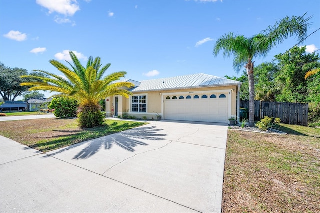 ranch-style home with driveway, metal roof, fence, a garage, and stucco siding