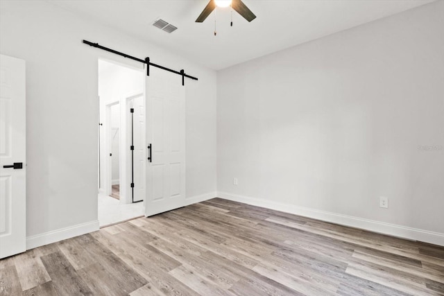 3851 W Wilburton Dr, Citrus Springs, FL 34433 - unfurnished bedroom featuring a barn door, ceiling fan, visible vents, baseboards, and wood finished floors