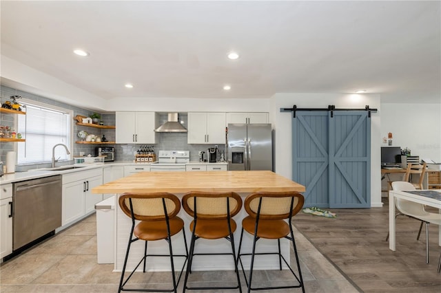 kitchen featuring wall chimney range hood, open shelves, a sink, a barn door, and stainless steel appliances