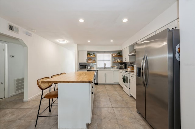 kitchen with a sink, stainless steel appliances, open shelves, visible vents, and wooden counters