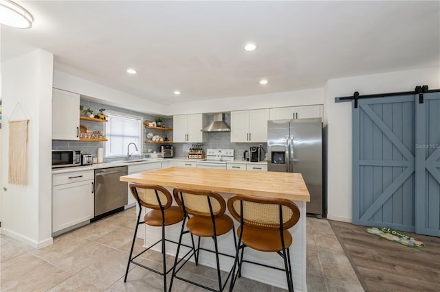 kitchen featuring open shelves, appliances with stainless steel finishes, white cabinets, a sink, and wall chimney exhaust hood