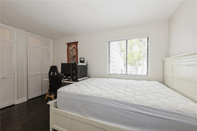 bedroom featuring baseboards, multiple closets, and dark wood-type flooring