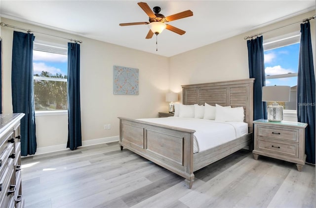 bedroom with light wood-style floors, baseboards, ceiling fan, and multiple windows