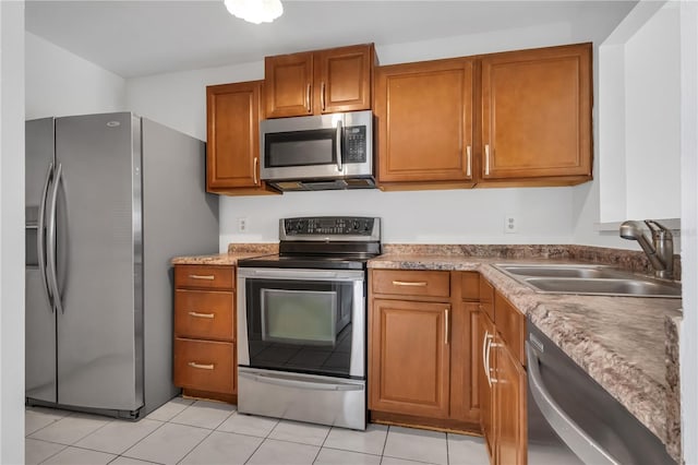 kitchen featuring a sink, appliances with stainless steel finishes, light tile patterned flooring, and brown cabinets