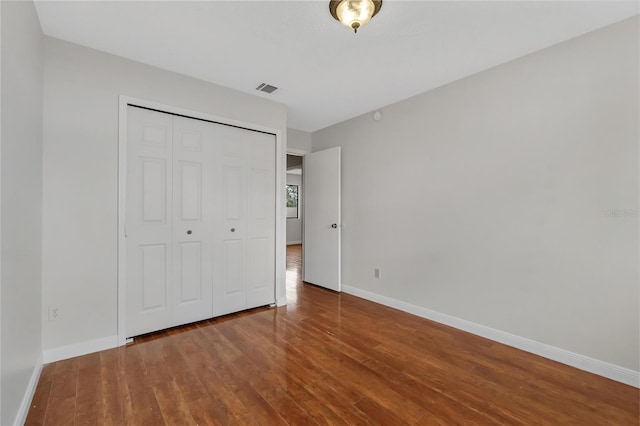 unfurnished bedroom featuring baseboards, visible vents, wood finished floors, and a closet