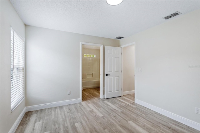 spare room with a textured ceiling, visible vents, light wood-style flooring, and baseboards