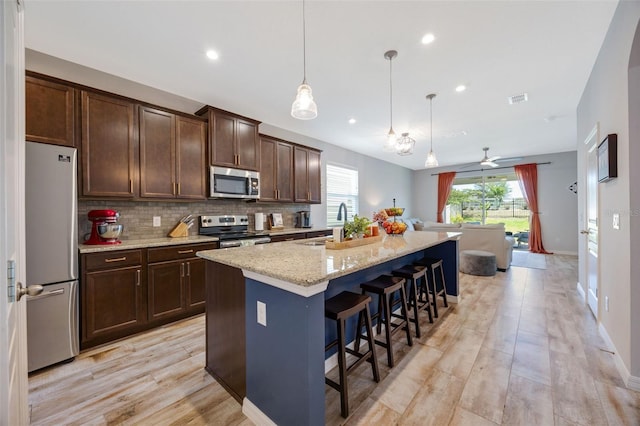 kitchen with a center island with sink, visible vents, dark brown cabinetry, light stone counters, and appliances with stainless steel finishes