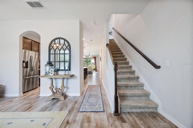 foyer entrance featuring stairs, arched walkways, light wood-style flooring, baseboards, and visible vents