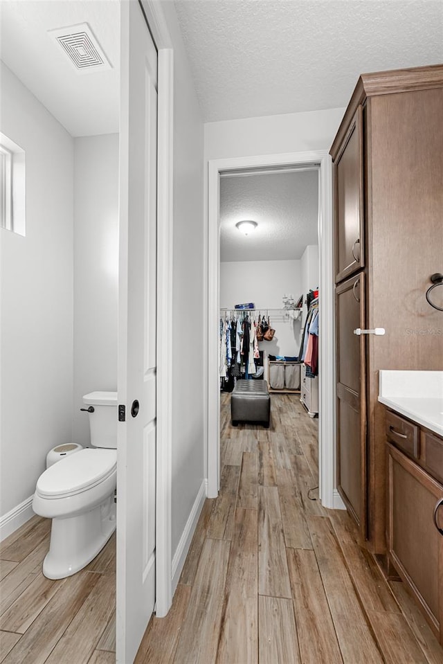 42368 W Cashew Ct, Eustis, FL 32736 - bathroom with toilet, visible vents, a textured ceiling, wood finished floors, and a spacious closet