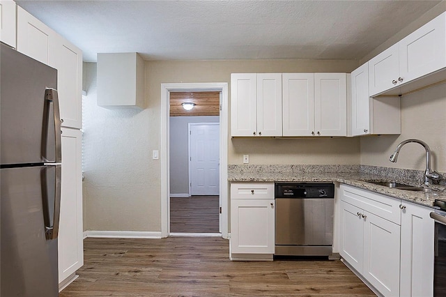 kitchen with stainless steel appliances, white cabinetry, a sink, and wood finished floors