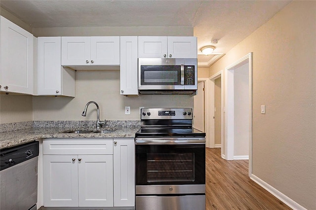 kitchen with wood finished floors, a sink, baseboards, stainless steel appliances, and white cabinetry