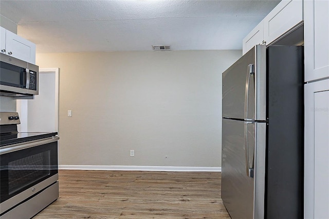 kitchen featuring white cabinetry, appliances with stainless steel finishes, light wood-style flooring, and visible vents