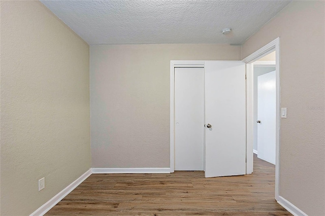 unfurnished room featuring baseboards, a textured ceiling, a textured wall, and wood finished floors