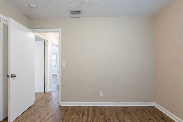 empty room featuring baseboards, a textured ceiling, wood finished floors, and visible vents