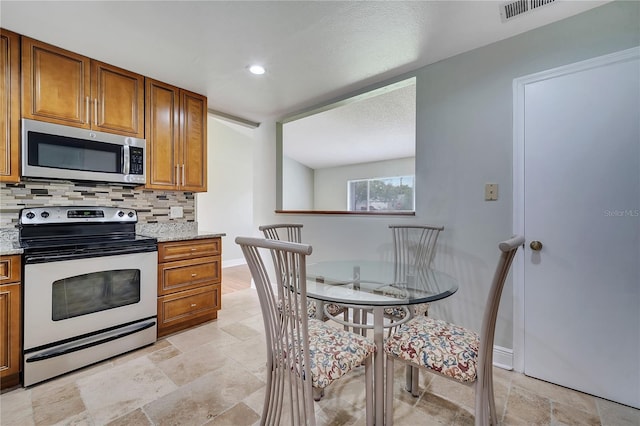 819 Haulover Dr, Altamonte Springs, FL 32714 - kitchen with stainless steel microwave, range with electric stovetop, stone tile flooring, brown cabinets, and backsplash