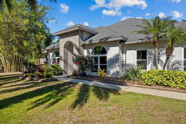 mediterranean / spanish house with stucco siding, a shingled roof, and a front lawn