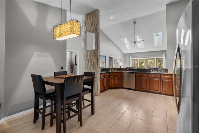 kitchen featuring brown cabinets, appliances with stainless steel finishes, dark countertops, high vaulted ceiling, and a skylight