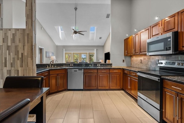 kitchen featuring a sink, high vaulted ceiling, ceiling fan, a skylight, and appliances with stainless steel finishes