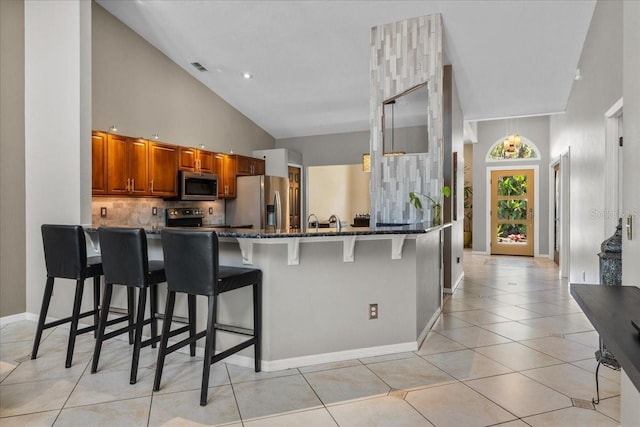 kitchen with dark stone counters, a breakfast bar area, brown cabinetry, stainless steel appliances, and a peninsula