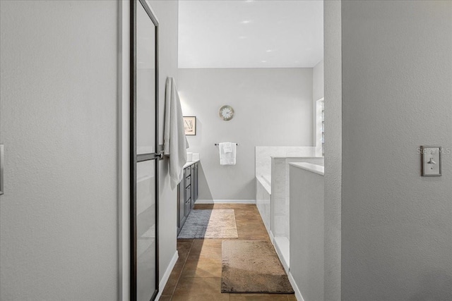 full bath with vanity, tile patterned floors, a textured wall, baseboards, and a garden tub