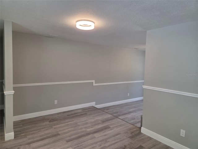 unfurnished room with baseboards, wood finished floors, and a textured ceiling