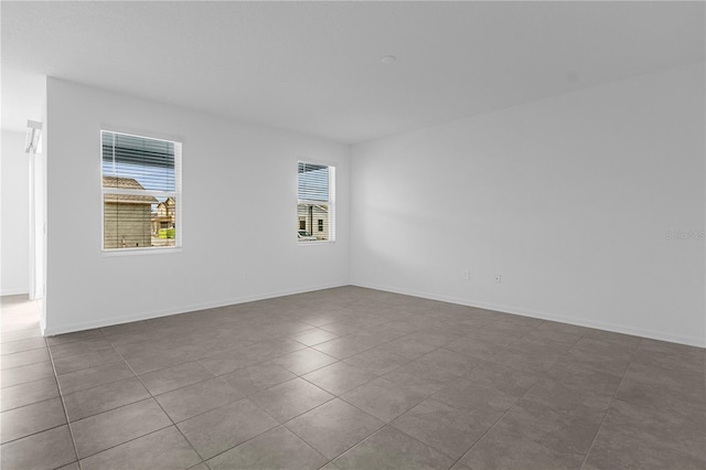 unfurnished room with baseboards and dark tile patterned floors