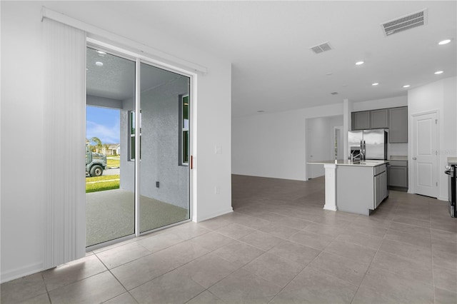 kitchen with recessed lighting, visible vents, gray cabinets, a kitchen island with sink, and stainless steel refrigerator with ice dispenser