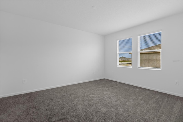 unfurnished room with baseboards and dark carpet