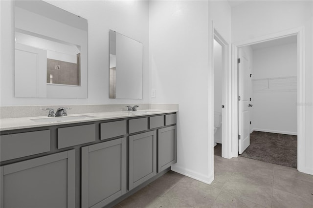 full bath featuring tile patterned floors, double vanity, a sink, a walk in closet, and baseboards