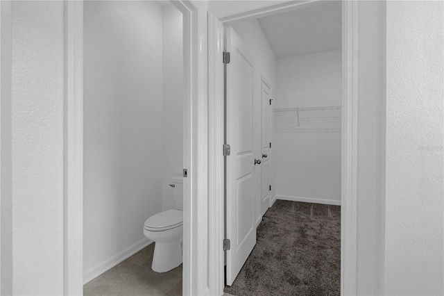 bathroom featuring a walk in closet, toilet, and baseboards